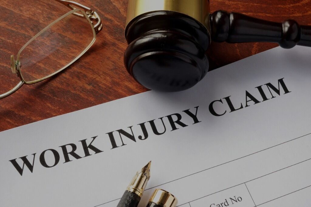A gavel and eyeglasses resting on a 'WORK INJURY CLAIM' form, symbolizing the Office of Workers’ Compensation Programs (OWCP) legal services.